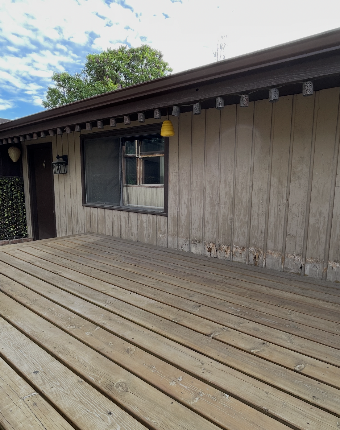Weathered back deck with peeling siding and bare wood boards before painting