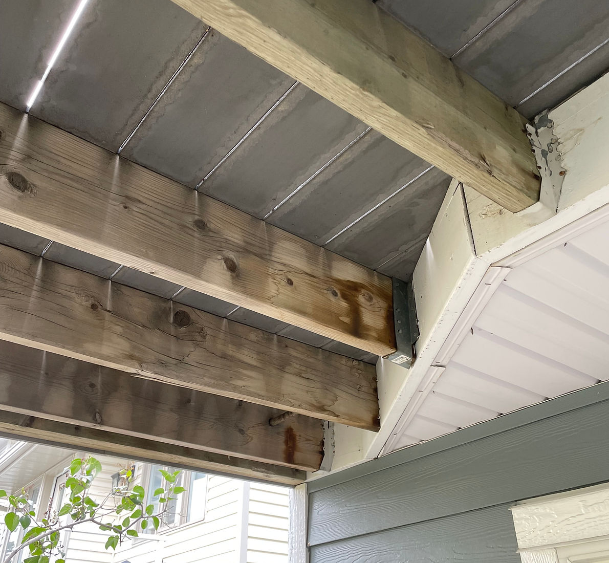 Bare wood deck beams under a covered porch before painting